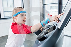 Adorable kid girl in sportswear training on treadmill at gym
