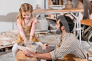 adorable kid making ceramic pot on pottery wheel with teacher