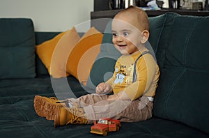 Adorable kid smiling while sitting on green couch with yellow cushions