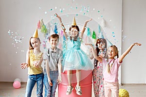 Adorable kids have fun together, throw colourful confetti, wears cone hats, have fun at birthday party, play together in