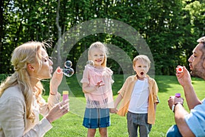 adorable kids holding hands and looking at parents blowing soap bubbles