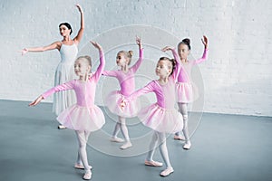 adorable kids in pink tutu skirts practicing ballet with young teacher