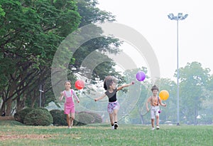 Adorable kids play together with cheerful and very enjoyable, children hold colorful balloons in hand and competitive run in green