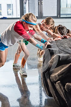 Adorable kids in sportswear training with tire at fitness studio