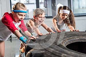 Adorable kids in sportswear training with tire at fitness studio