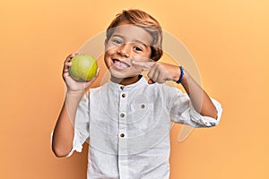 Adorable latin kid holding green apple smiling happy pointing with hand and finger