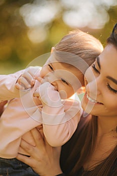 Adorable laughing baby girl on mom`s hands in autumn park. Close up on mother and daughter. Happy family