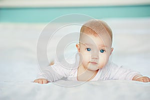 Adorable laughing baby in white sunny bedroom. Newborn infant child relaxing in bed. Textile for kids. Family morning at home. Fam