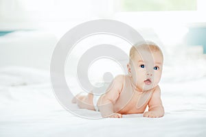 Adorable laughing baby in white sunny bedroom. Newborn infant child relaxing in bed. Textile for kids. Family morning at home. Fam