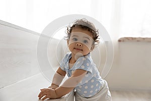 Adorable little african baby relying on furniture, making first steps.