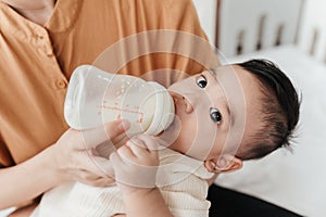 Adorable little Asian baby drinking milk from baby bottle. Mother holding adorable her son with milk feeding from milk bottle.