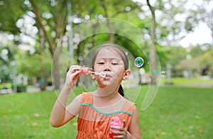 Adorable little Asian child girl blowing soap bubbles in green garden