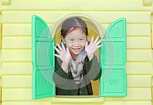 Adorable little Asian child girl playing with window toy playhouse in playground