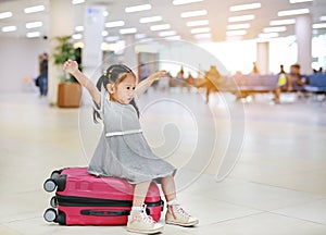 Adorable little asian girl at airport sitting on suitcase with open arm