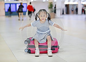 Adorable little asian girl at airport sitting on suitcase with open arm