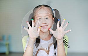 Adorable little Asian girl with colorful fingers painted in the children room