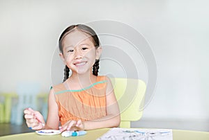 Adorable little Asian girl drawing and painting with water color on paper in children room with looking at camera