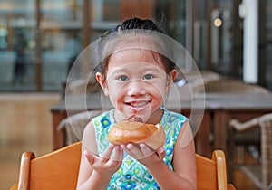 Adorable little Asian girl eating bread. Child having breakfast