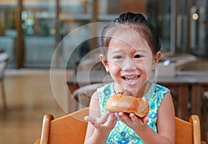 Adorable little Asian girl eating bread. Child having breakfast