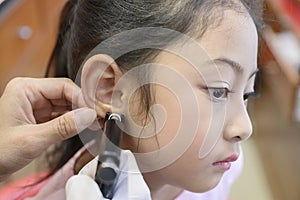 Adorable little Asian girl having ear piercing process.