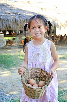 Adorable little asian girl holding a basket with eggs outdoors in the farms