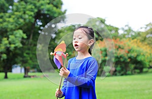 Adorable little Asian kid girl blowing wind turbine in the summer garden