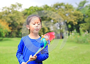 Adorable little Asian kid girl blowing wind turbine in the summer garden