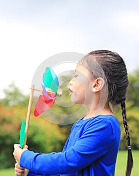 Adorable little Asian kid girl blowing wind turbine in the summer garden