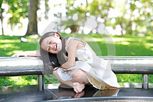 Adorable little Asian kid girl sitting on bench in sunny green park