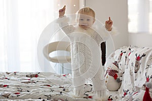 Adorable little baby boy in handknitted overall, eating cookies