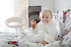 Adorable little baby boy in handknitted overall, eating cookies