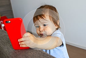 Adorable little baby boy looking seriously at screen of mobile phone.