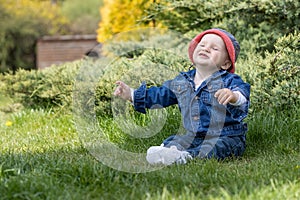 Adorable little baby boy is relaxing sitting on the grass outdoors