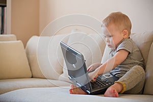 Adorable little baby boy sitting on a sofa and playing with toy computer. Cute little childs feet, boy playing