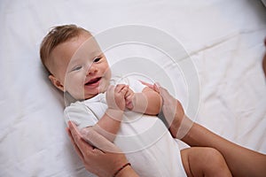 Adorable little baby boy in white bodysuit lying on the bed and connecting with his mother, smiling looking at her