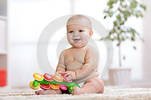 Adorable little baby in diaper sits on carpet and plays with toy at home. Shallow depth of field.