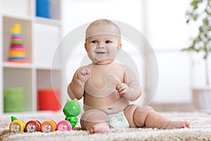 Adorable little baby in diaper sits on carpet and plays with toy at home. Shallow depth of field.