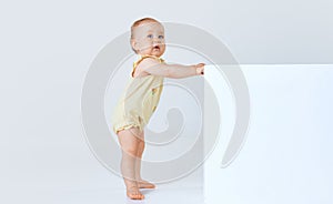 Adorable little baby girl, child, toddler in comfortable cute clothes standing and looking against grey studio