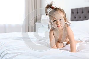 Adorable little baby girl crawling on bed in room