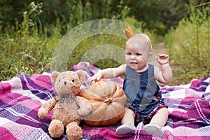 Adorable little baby girl having fun with pumpkin and toy teddy bear on beautiful autumn day outdoors. Happy child playing in