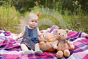 Adorable little baby girl having fun with pumpkin and toy teddy bear on beautiful autumn day outdoors. Happy child playing in