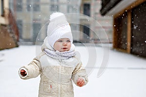 Adorable little baby girl making first steps outdoors in winter. Cute toddler learning walking.