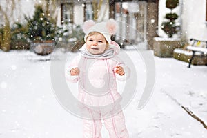 Adorable little baby girl making first steps outdoors in winter. Cute toddler learning walking.