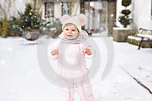 Adorable little baby girl making first steps outdoors in winter. Cute toddler learning walking