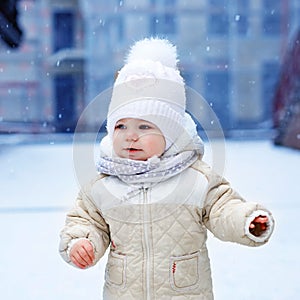 Adorable little baby girl making first steps outdoors in winter. Cute toddler learning walking. Child having fun on cold