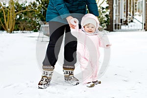 Adorable little baby girl making first steps outdoors in winter with mother. Cute toddler learning walking.