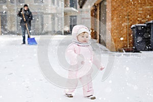 Adorable little baby girl making first steps outdoors in winter through snow. Cute toddler child learning walking. On