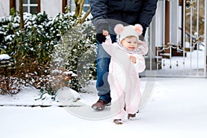 Adorable little baby girl making first steps outdoors in winter through snow. Cute toddler learning walking. Father