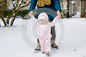 Adorable little baby girl making first steps outdoors in winter through snow. Cute toddler learning walking. Mother