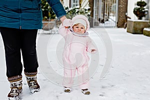 Adorable little baby girl making first steps outdoors in winter through snow. Cute toddler learning walking. Mother